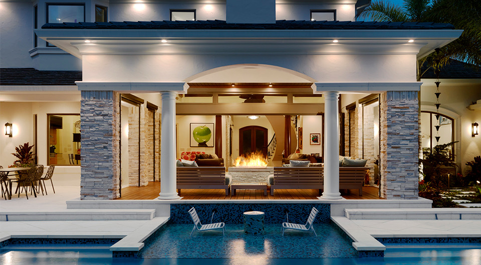 A Fechtel Company home at dusk: a stone-columned lanai, a fire feature, and the pool lit for the evening